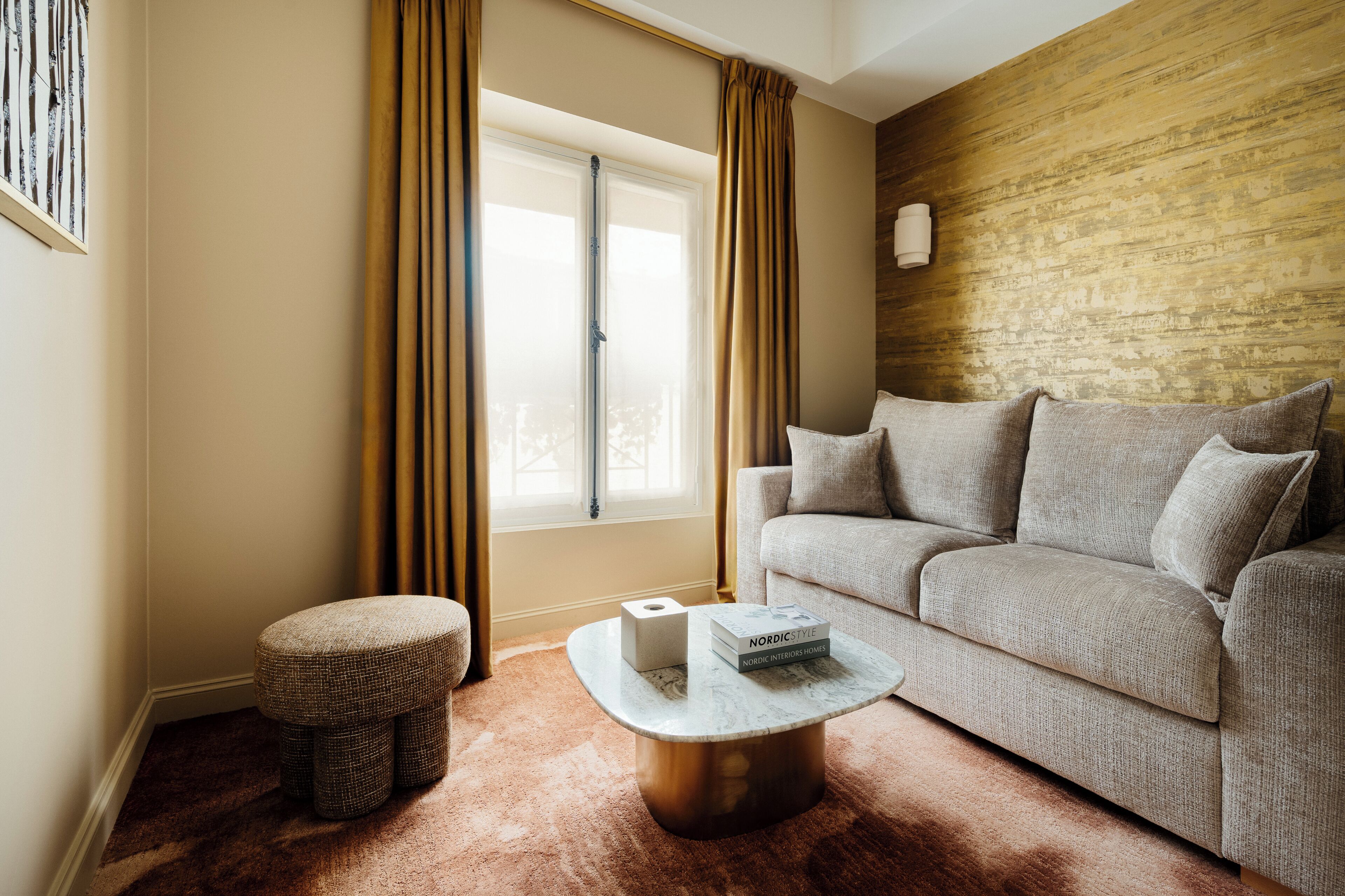 A living room with a sofa, a coffee table, a small ottoman, and a window with curtains.