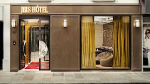 The exterior of JILS HOTEL with a red carpet entrance, a large glass door, and a visible interior with a sofa and curtains. - Jills Hotel (Paris)