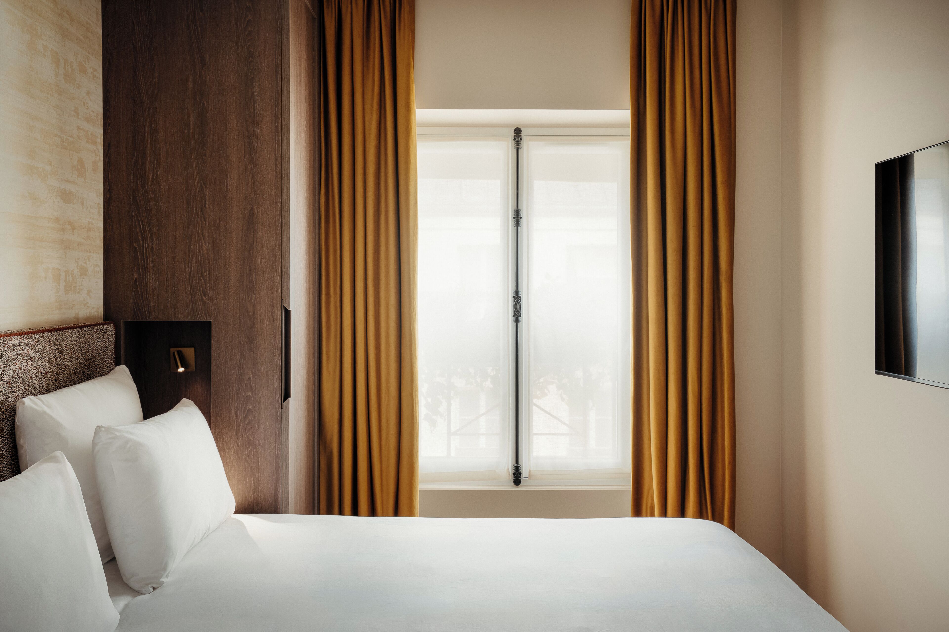 A hotel room with a bed, curtains, a window, and a wall-mounted TV.