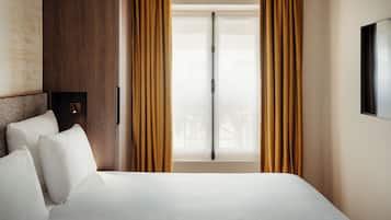 Habitación de hotel con cama, cortinas, una ventana y televisor montado en la pared.