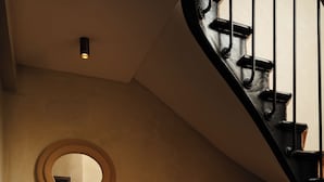 A spiral staircase with a wooden handrail and black balusters, a wavy mirror on the wall, and a light fixture above. - Jills Hotel (Paris)
