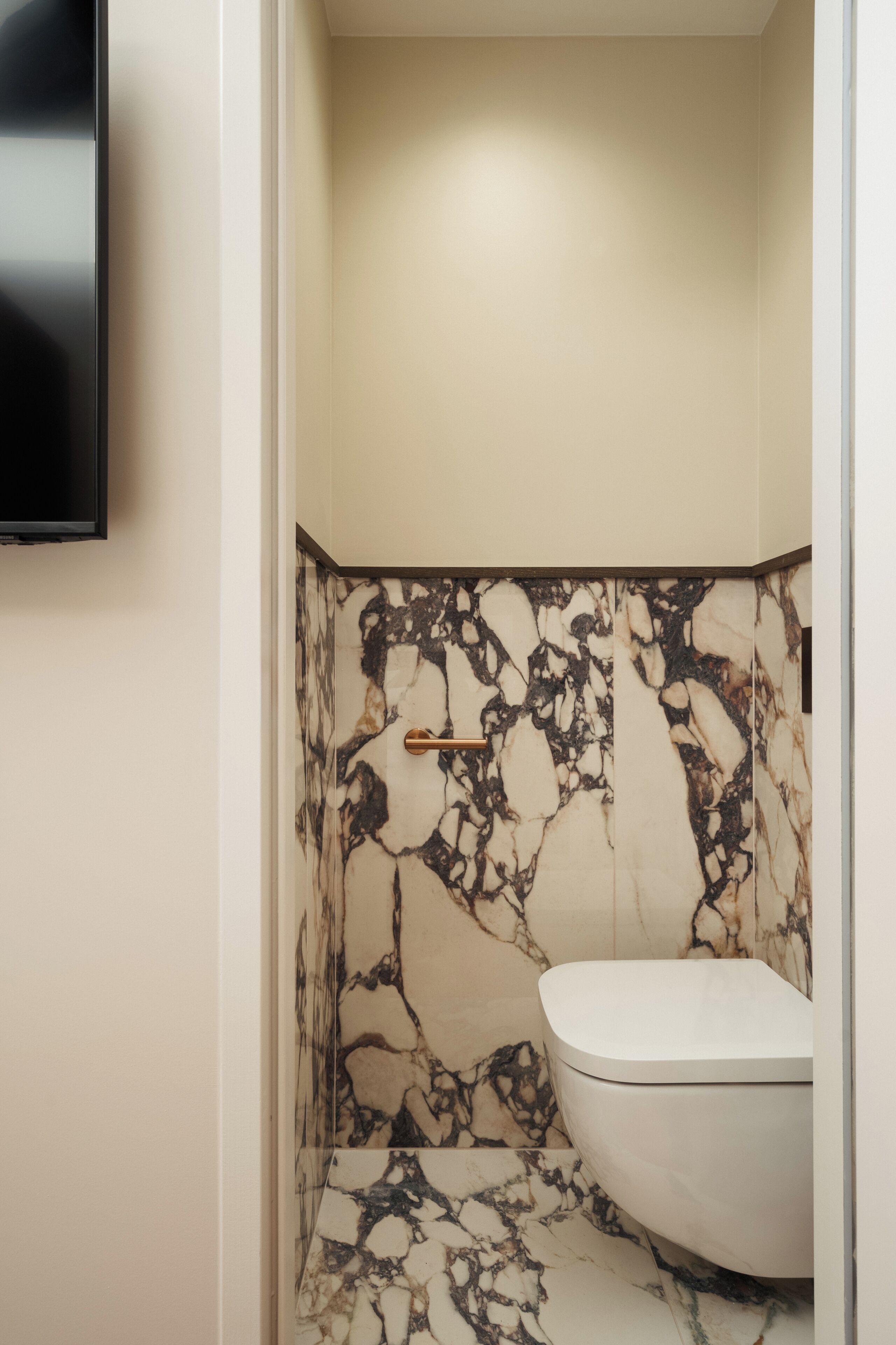 Un baño con pared de mármol, inodoro y televisor montado.