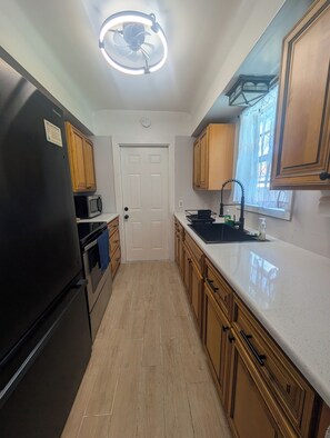 A kitchen with wooden cabinets, a black refrigerator, a microwave, and a stainless steel sink. - Recently Renovated• Coastal Getaway • Pet-Friendly (Hudson)