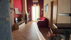 Un amplio salón con piso de baldosas, un sofá rojo, un banco de madera y un televisor sobre un mueble.