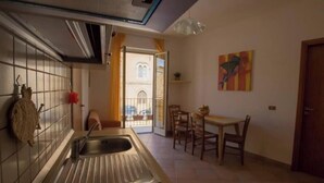 Una cocina compacta con un lavamanos, una zona de comedor con sillas y vistas a un edificio a través de una puerta abierta.