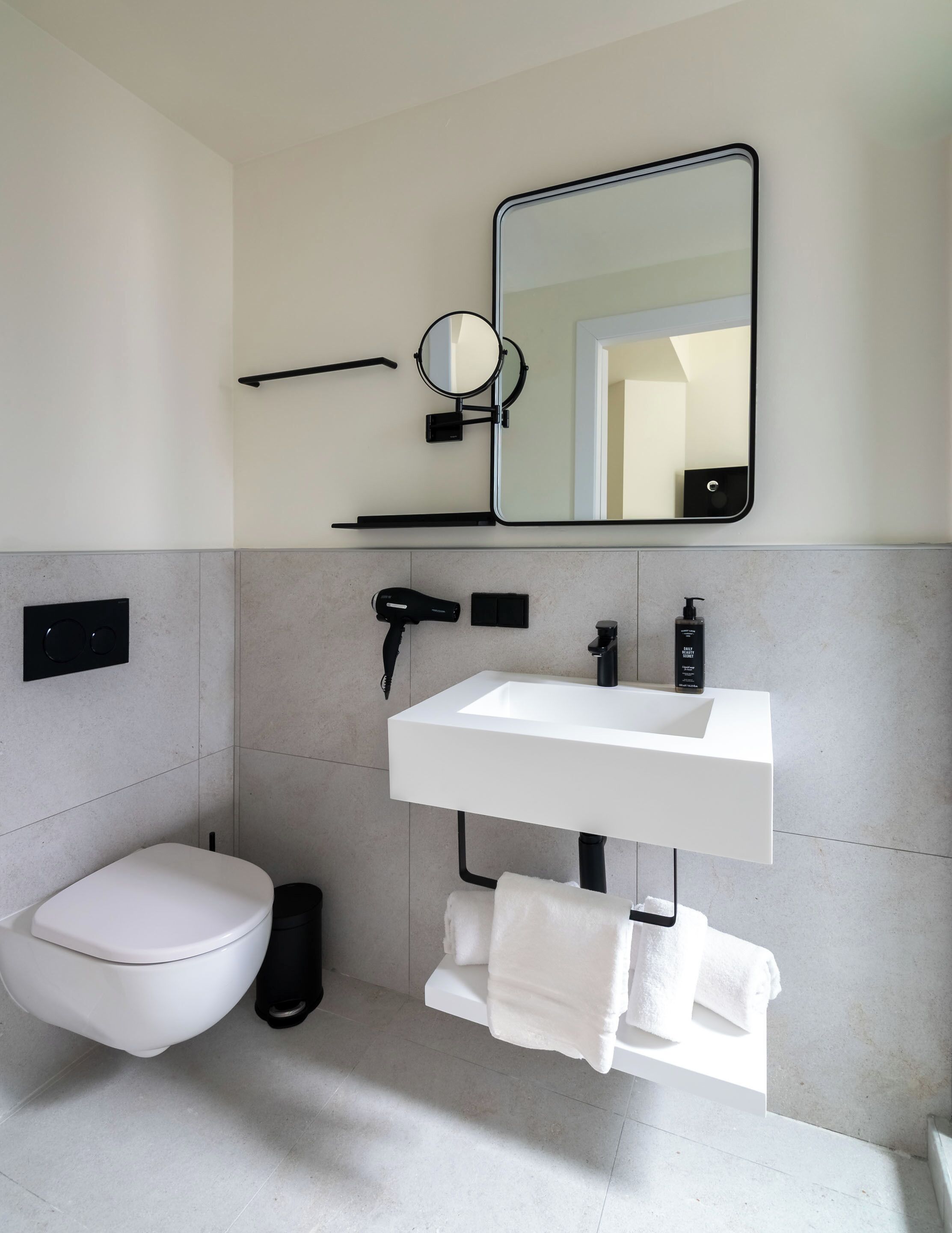 Een moderne badkamer met een wit toilet, een wastafel met spiegel erboven en een handdoekrek.