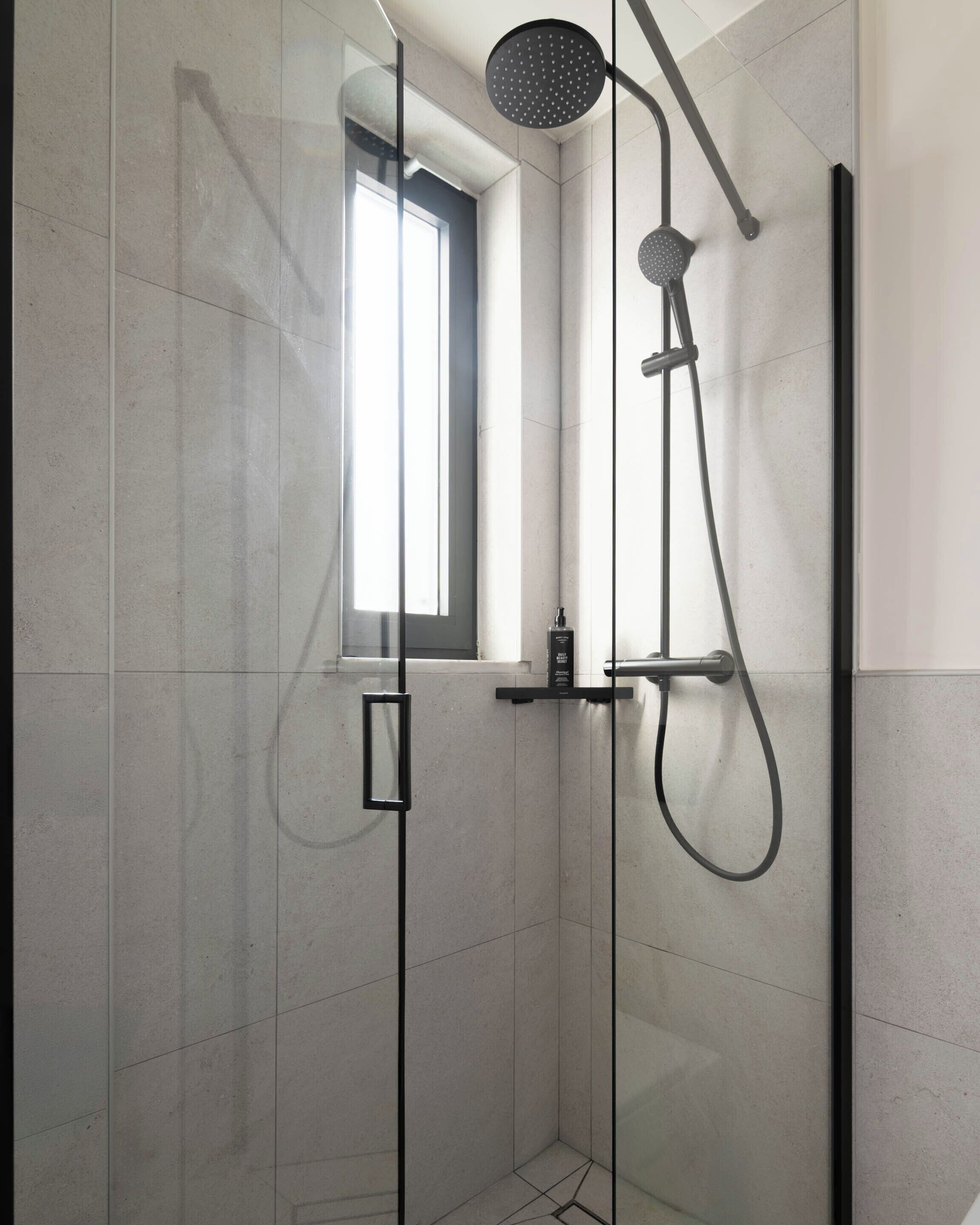 A modern shower enclosure with a glass door, a handheld showerhead, and a wall-mounted faucet.