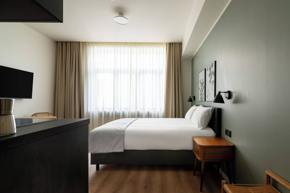 A hotel room with a bed, bedside table, and a TV on a dresser.
