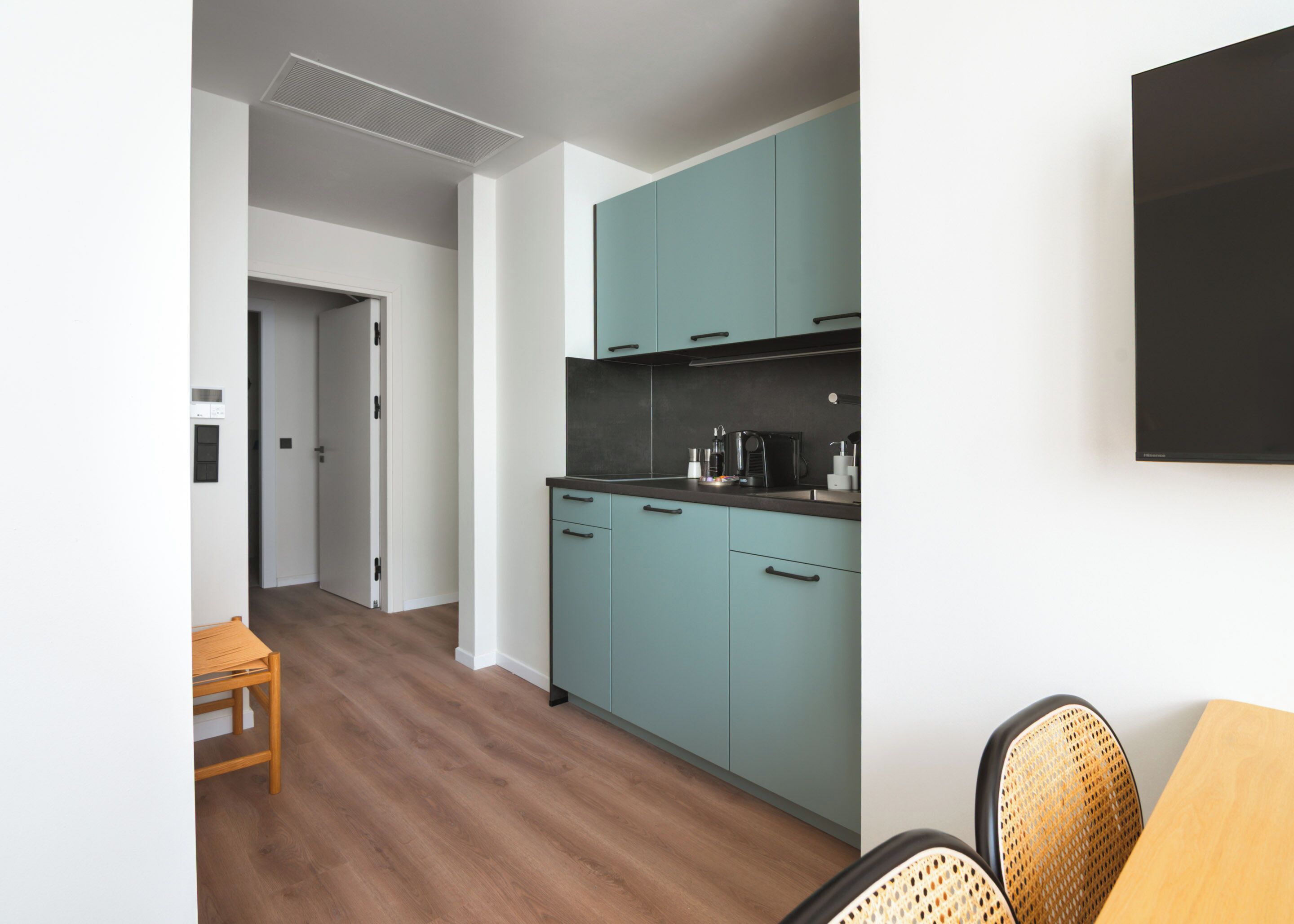 A modern kitchen with teal cabinets, a wooden dining table, and a black coffee machine.
