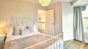 Een slaapkamer met een bed met een wit metalen frame, een geweven deken en een hanglamp.