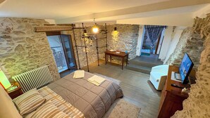 Une chambre avec un mur en pierre, un lit avec une literie à rayures, une table en bois et un téléviseur.