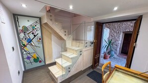 Un intérieur moderne avec un escalier, une porte en verre ornée d’une œuvre d’art abstraite et une table en bois.