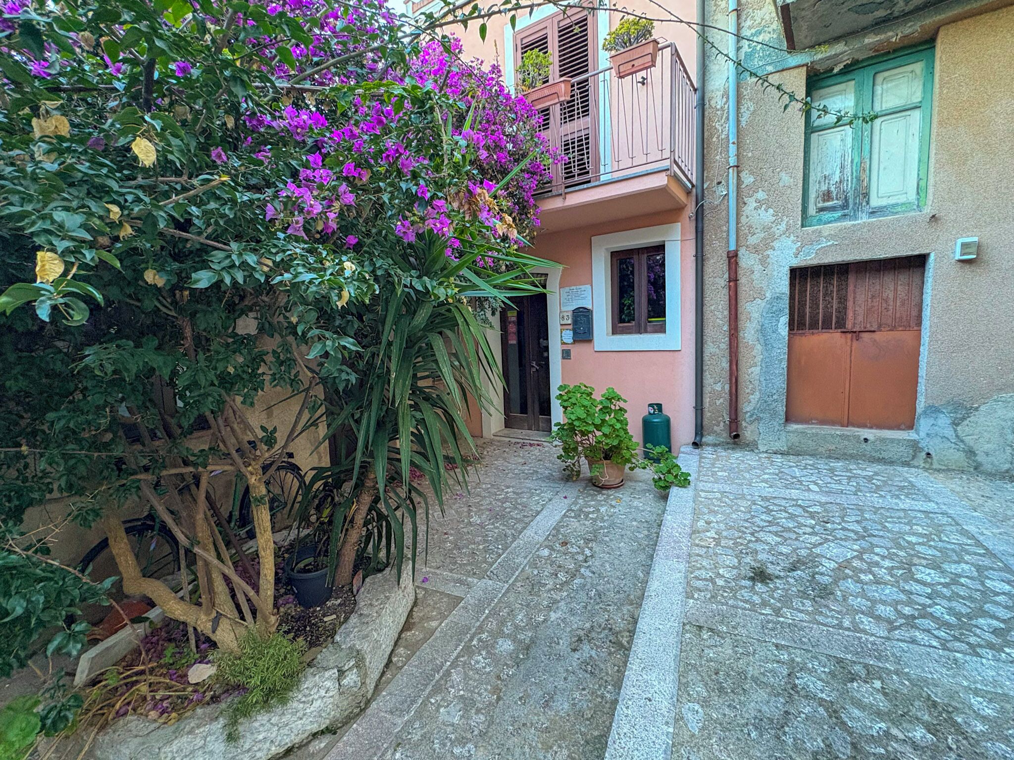 Une ruelle étroite pavée, bordée d’un immeuble doté d’un balcon avec une balustrade en métal et d’une porte.