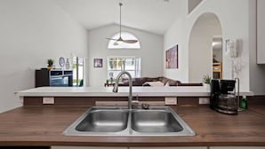 A modern kitchen with a double sink, a coffee maker, and a dining area with a sofa. - Sunshine Serenity Villa (Kissimmee)