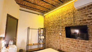 A hotel room with a brick wall, a bed, a TV mounted on the wall, and a shelf with towels. - Karaköy Port House  (Istanbul)