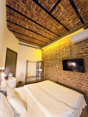 A hotel room with a brick wall, a bed, a TV mounted on the wall, and a shelf with towels. - Karaköy Port House (Istanbul)