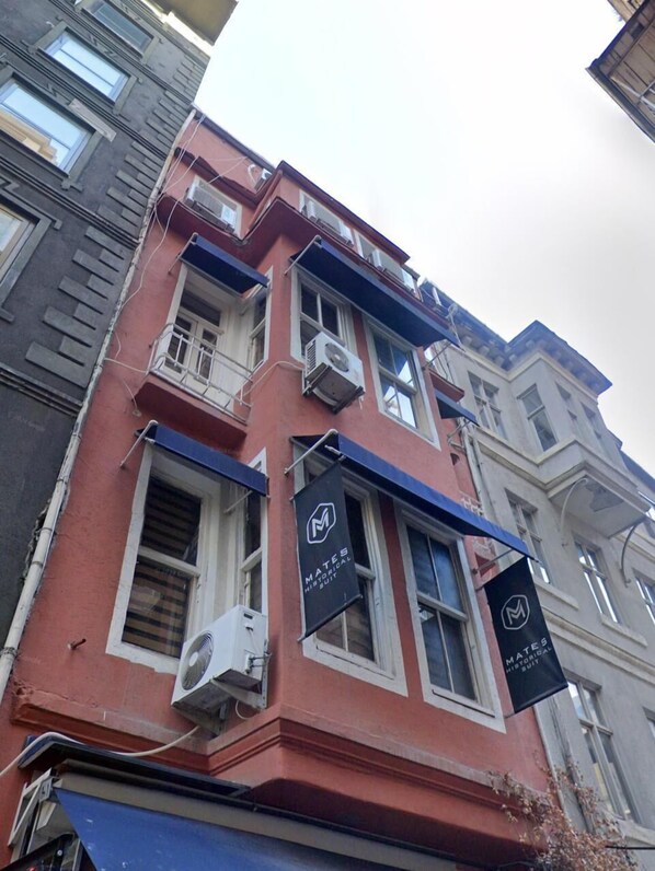 A multi-story building with a red facade, air conditioning units, and two banners advertising 'Mates Historical Suit'. - Karaköy Port House (Istanbul)