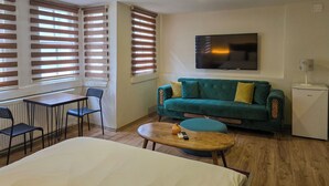 En moderne stue med en turkis sofa, et lille sofabord, et fjernsyn monteret på væggen og et kompakt køleskab.