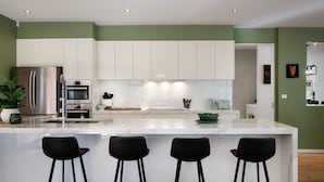 Una cucina moderna con mobili bianchi, elettrodomestici in acciaio inossidabile e un'isola centrale con sgabelli da bar.