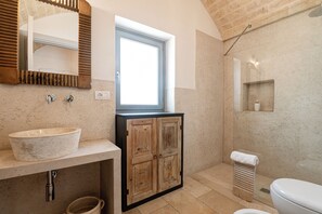 Een badkamer met een groot raam, een houten kastje, een wastafel en een douchehoek.