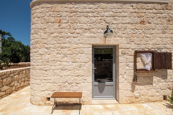 Un bâtiment en pierre avec une porte, un banc et une lampe.