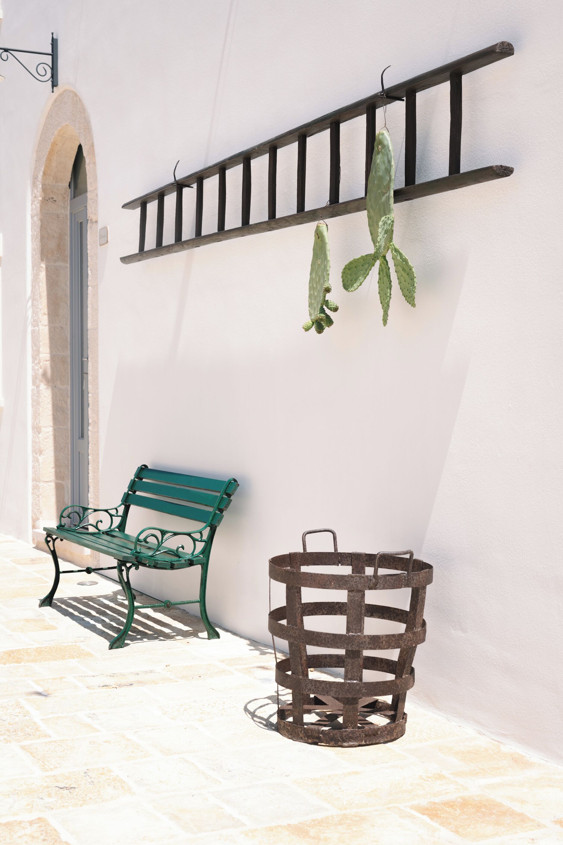A green bench and a metal basket against a white wall with a metal rack above.