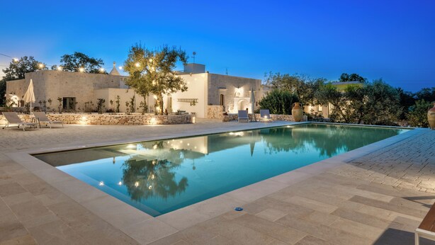 A swimming pool with lounge chairs and a stone wall. - Borgo Altobello (Cisternino)