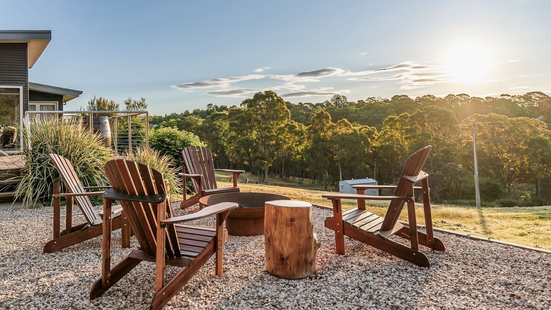 An outdoor seating area with Adirondack chairs and a central wooden table, surrounded by gravel.