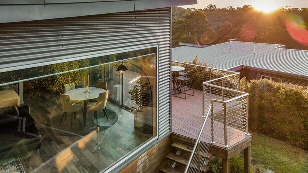 Una casa moderna con un patio de cristal, zona de comedor y terraza de madera.