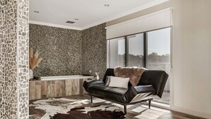 Un baño moderno con paredes de mosaico, una bañera y un sillón de cuero negro con una manta de piel.