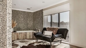 A modern bathroom with mosaic tile walls, a bathtub, and a black leather chair with a fur throw. - Frankie Luxury 2 bedroom house with Spa bath (Daylesford)