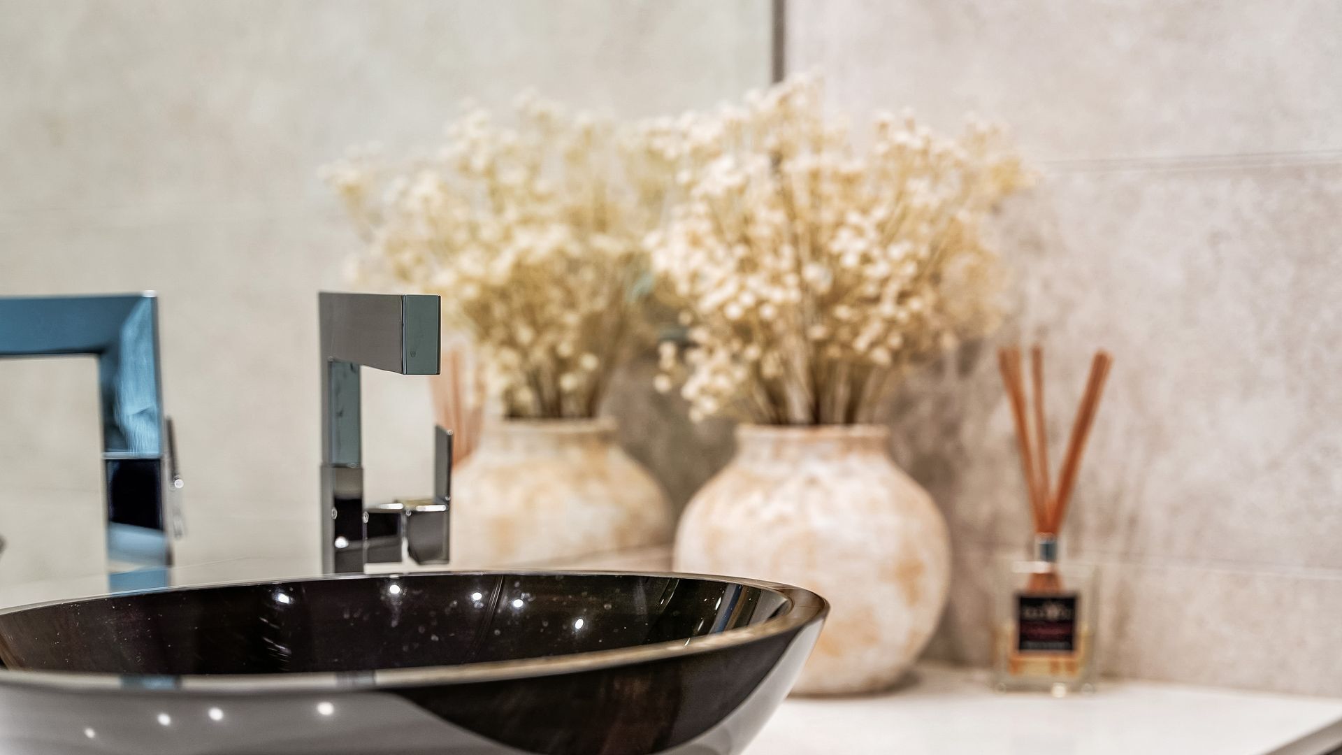Un baño moderno con un lavabo negro, un grifo azul y dos jarrones con flores secas.