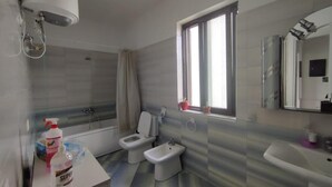 A modern bathroom with a bathtub, two toilets, a bidet, a sink, and a window providing natural light. - Tirana • 2 Single Beds • Free Wi-Fi • Pet-Friendly • Shared Kitchen & Bathroom (Tiarana)