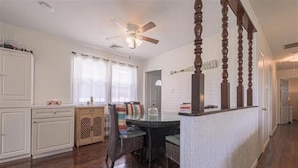 Una cocina amplia con muebles blancos, un comedor con una mesa redonda y sillas, y una escalera de madera con ventilador de techo.
