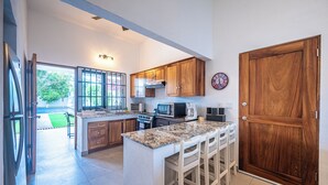 A modern kitchen with wooden cabinets, a granite countertop, and a large wooden door. - Casa Alegria Villa -Jaco Beach Great Location (Jacó)