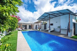 Una piscina con una veranda coperta, circondata da un prato curato e una casa con facciata bianca.