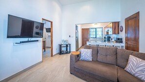 A modern living room with a brown sofa, a flat-screen TV mounted on the wall, and a kitchen in the background. - Casa Alegria Villa -Jaco Beach Great Location (Jacó)