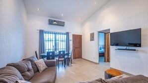 A modern living room with a brown sofa, dining table, and chairs. There is a TV mounted on the wall and a wooden door leading to another room. - Casa Alegria Villa -Jaco Beach Great Location (Jacó)