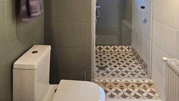 Un baño pequeño con inodoro, zona de ducha con azulejos estampados y una alfombra marrón en el suelo.