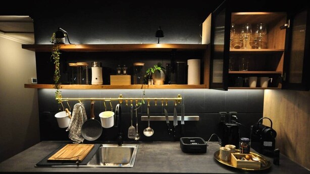 A modern kitchen with a stainless steel sink, hanging utensils, and a coffee machine.