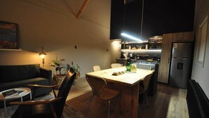 A modern kitchen with a dining area, wooden flooring, and a dark-colored sofa.
