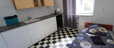 Une chambre avec un sol à carreaux, un lit recouvert d’une couette à motifs floraux, une table de chevet et une fenêtre avec des rideaux.