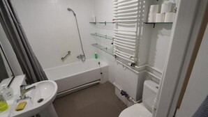 A bathroom with a bathtub, a sink, and a toilet. There are shelves with toiletries and a towel rack.