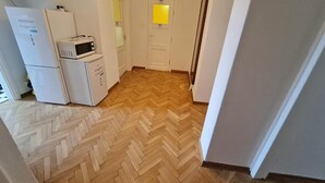A narrow hallway with a herringbone-patterned wooden floor, a white refrigerator, a microwave, and a door with a yellow window.