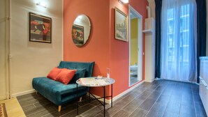 Ein Wohnzimmer mit einem petrolfarbenen Sofa, einem kleinen runden Tisch und einem Spiegel an der Wand.