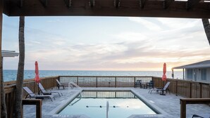 Ein Poolbereich mit Meerblick, einer Holzterrasse und Liegestühlen.