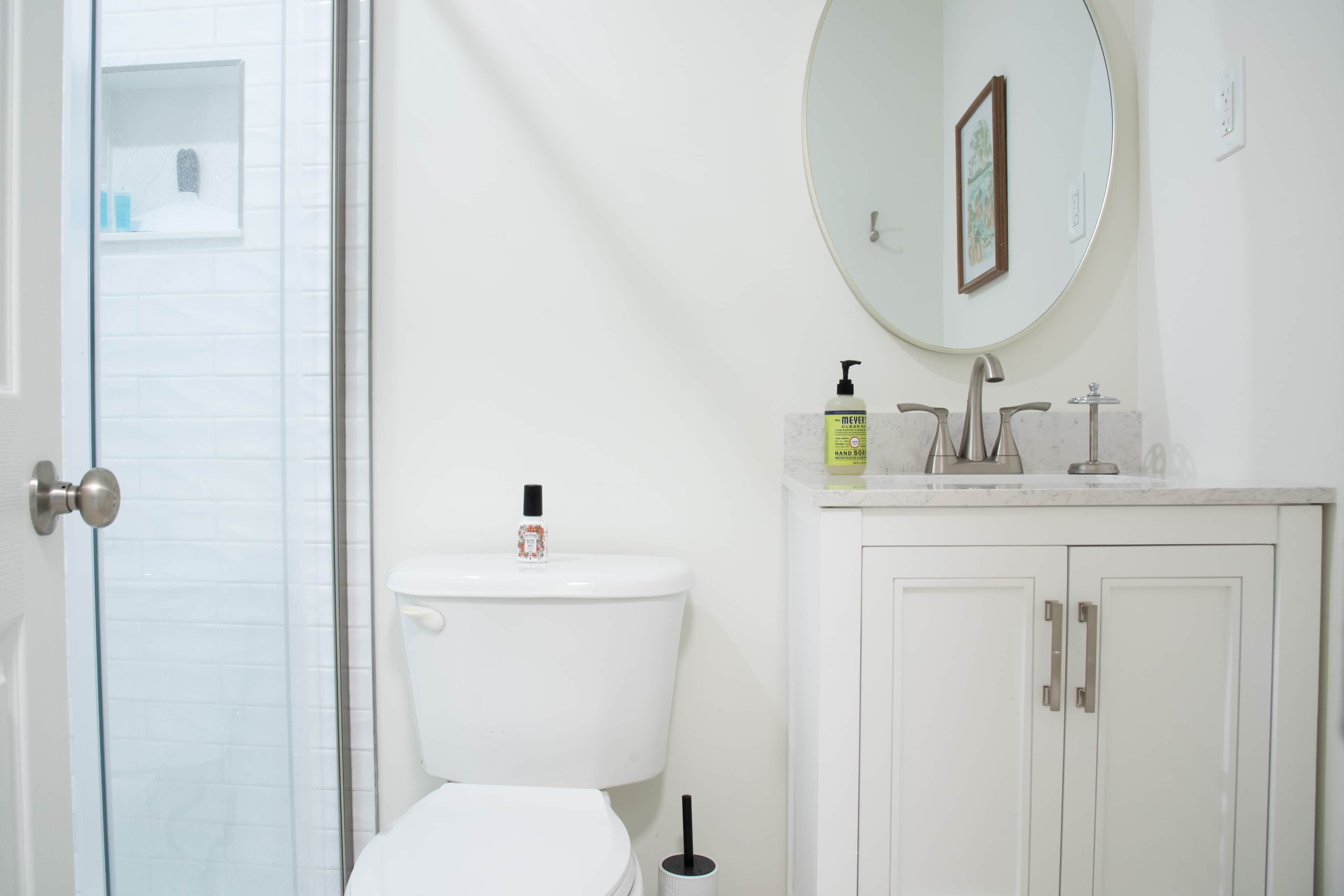 A bathroom with a toilet, a sink with a mirror, and a shower area.