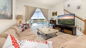 Sala de estar com sofá, TV e vista para uma piscina.