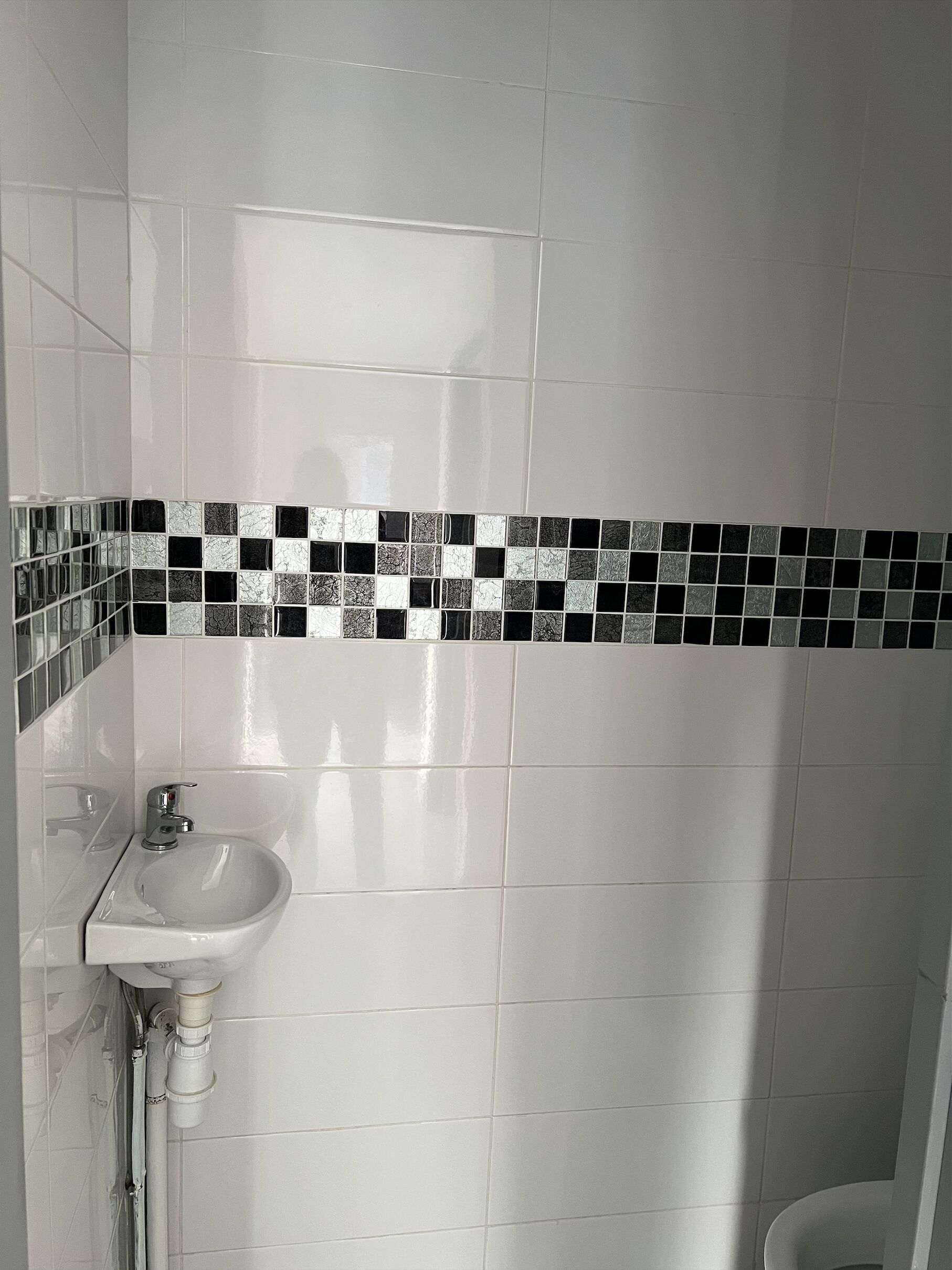 A bathroom with white tiles, a black and white mosaic border, and a white sink with a chrome faucet.