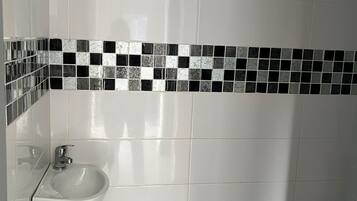 A bathroom with white tiles, a black and white mosaic border, and a white sink with a chrome faucet.